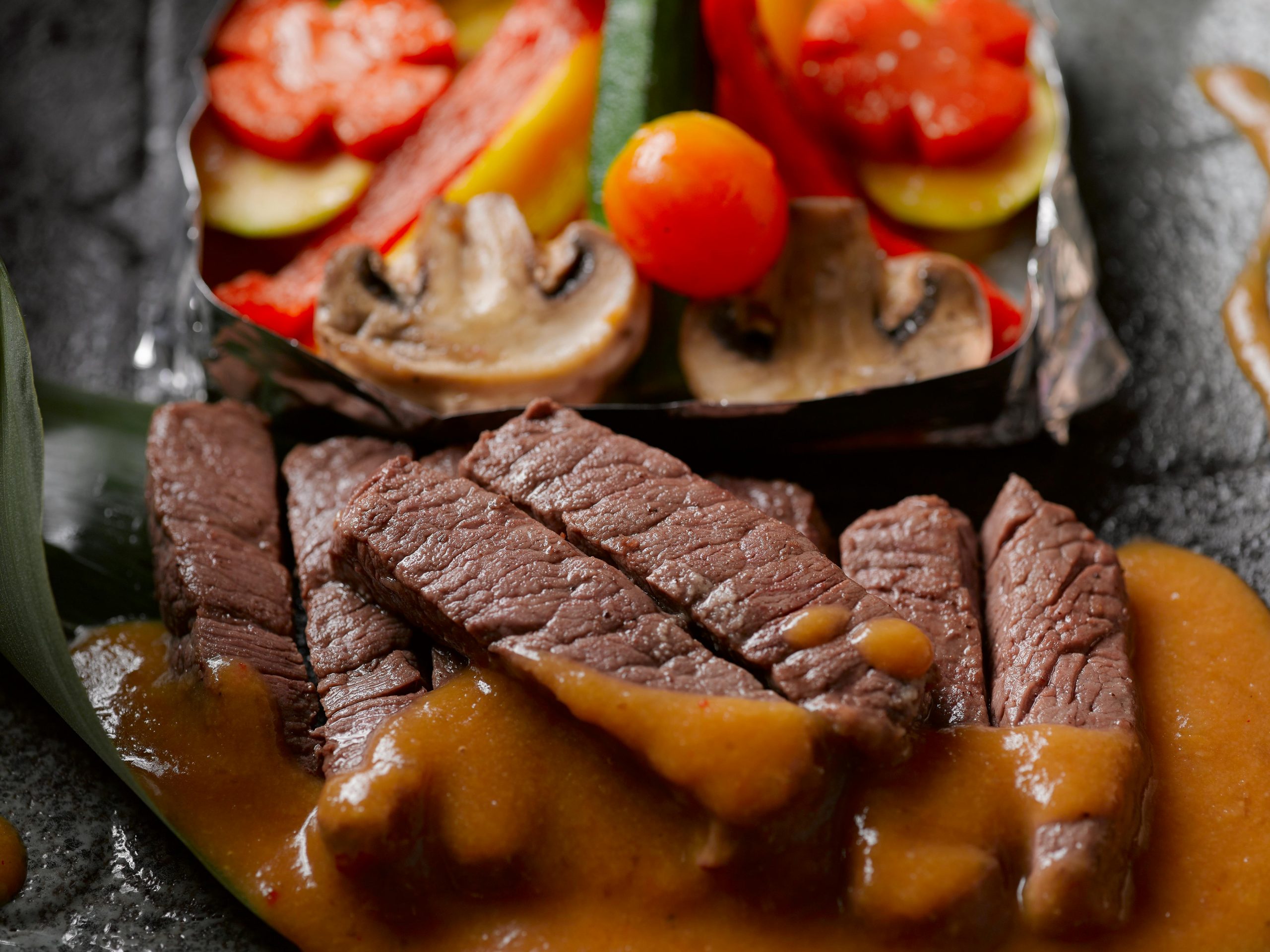 Succulent beef slices with savory sauce, paired with fresh grilled vegetables. Perfect gourmet meal.